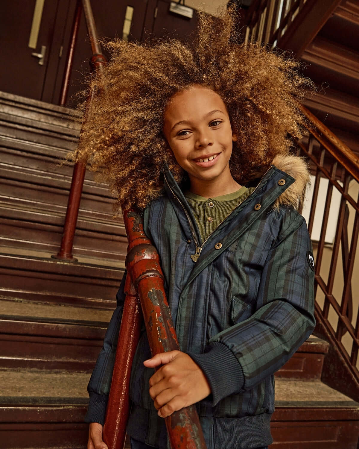 Black Watch Tartan City Transit Coat on a child standing on stairs, smiling and holding a railing.