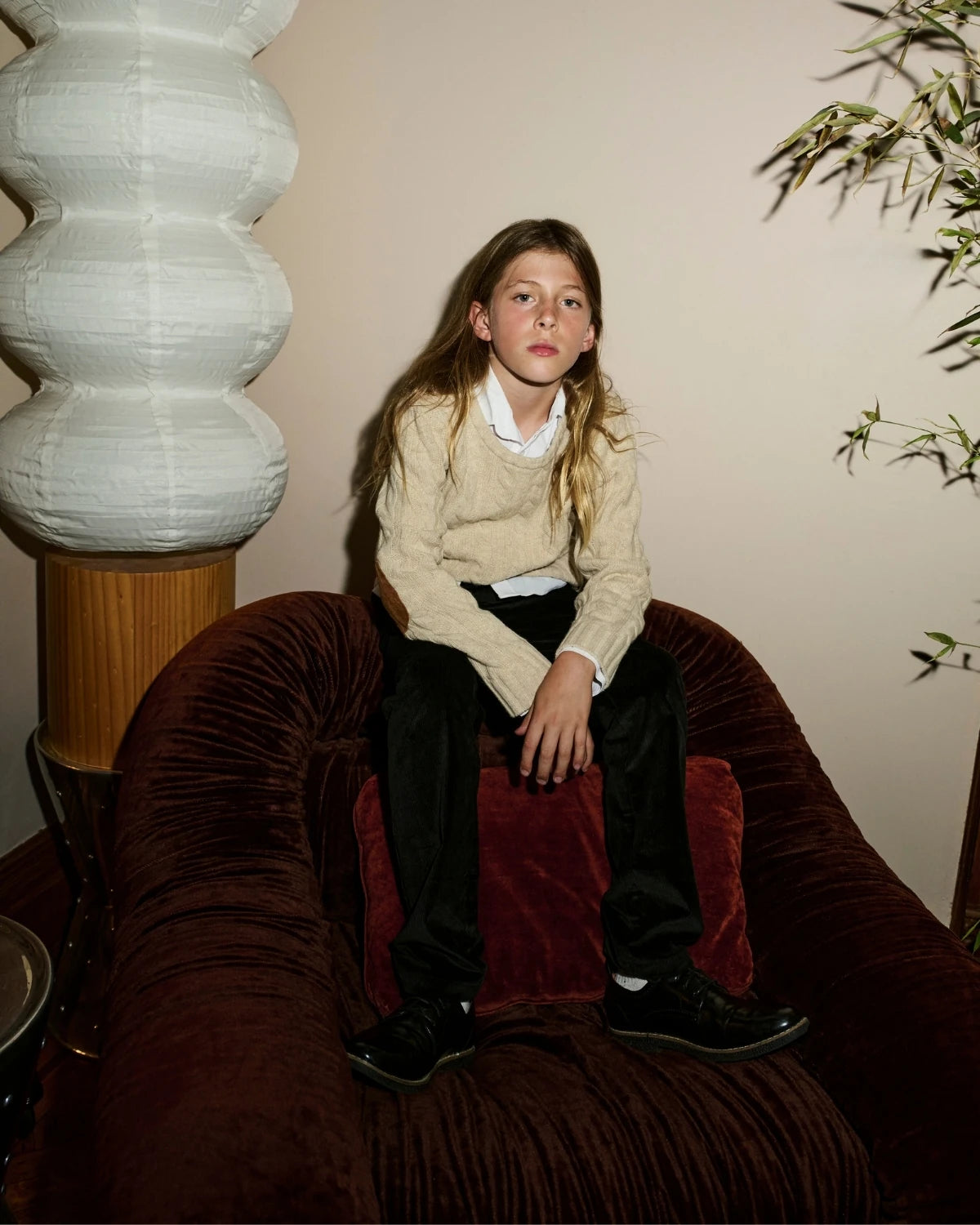 A girl wearing a cream sweater, seated on a velvet chair. Appaman Fall/Winter 2026 collection.