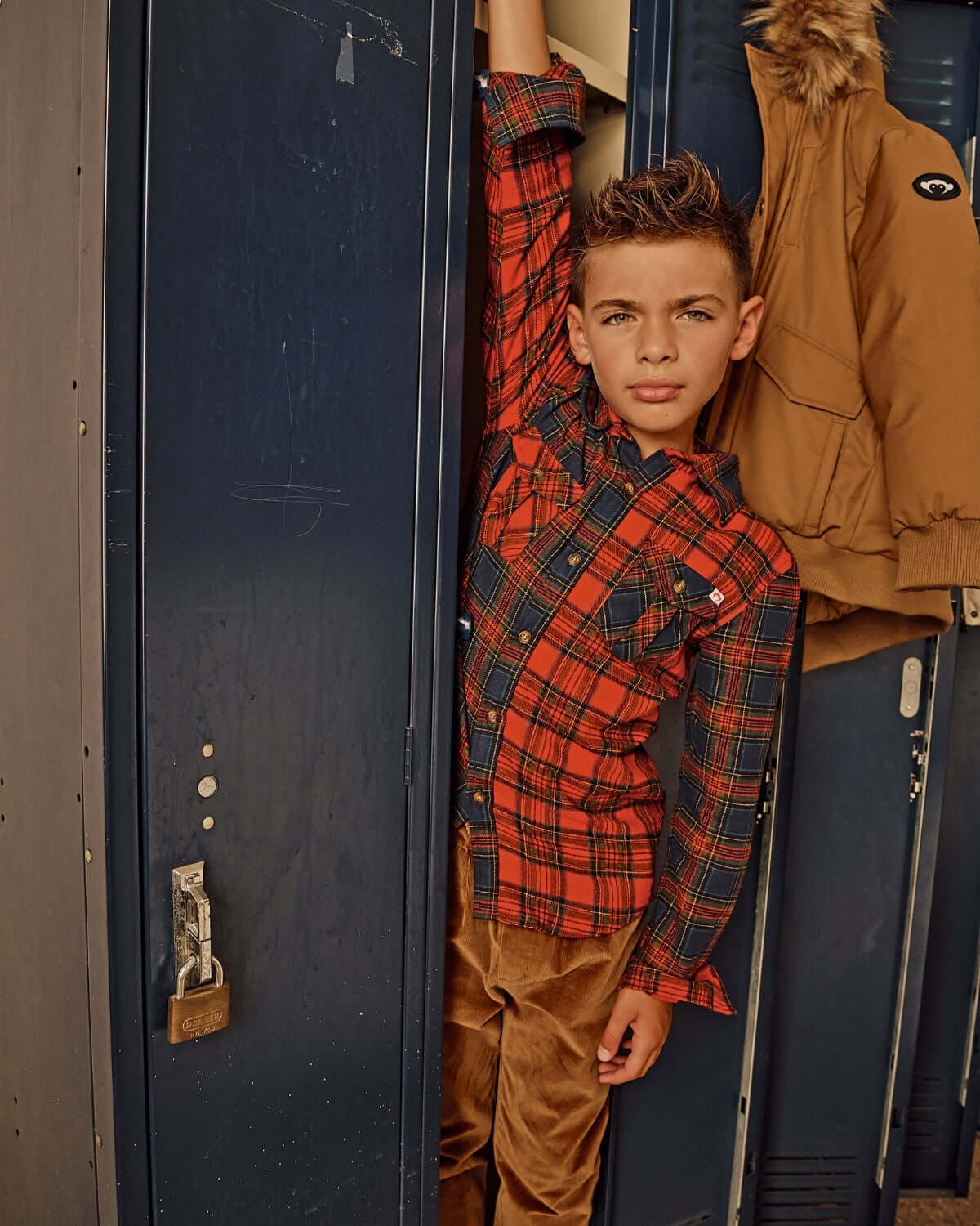 Boy wearing a red plaid shirt and British Khaki Cord Club Pants in a school locker setting.