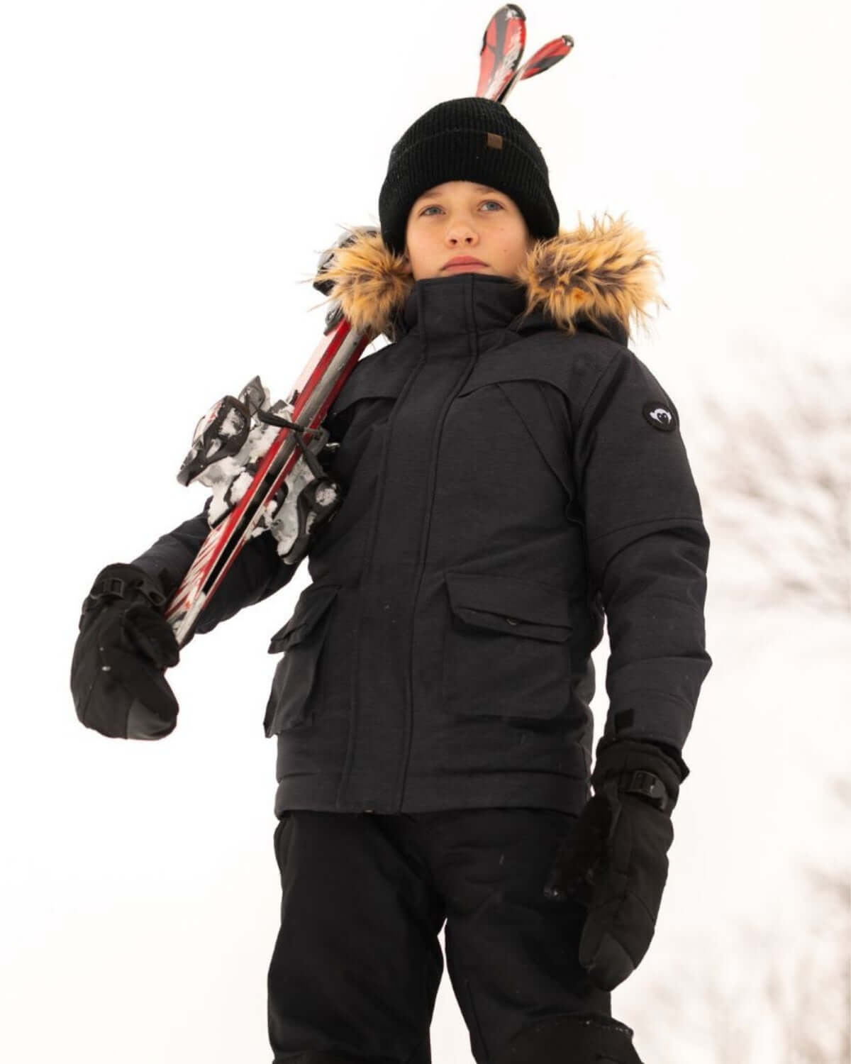Boy wearing Black Denali Down Coat with ski equipment in winter snow setting.