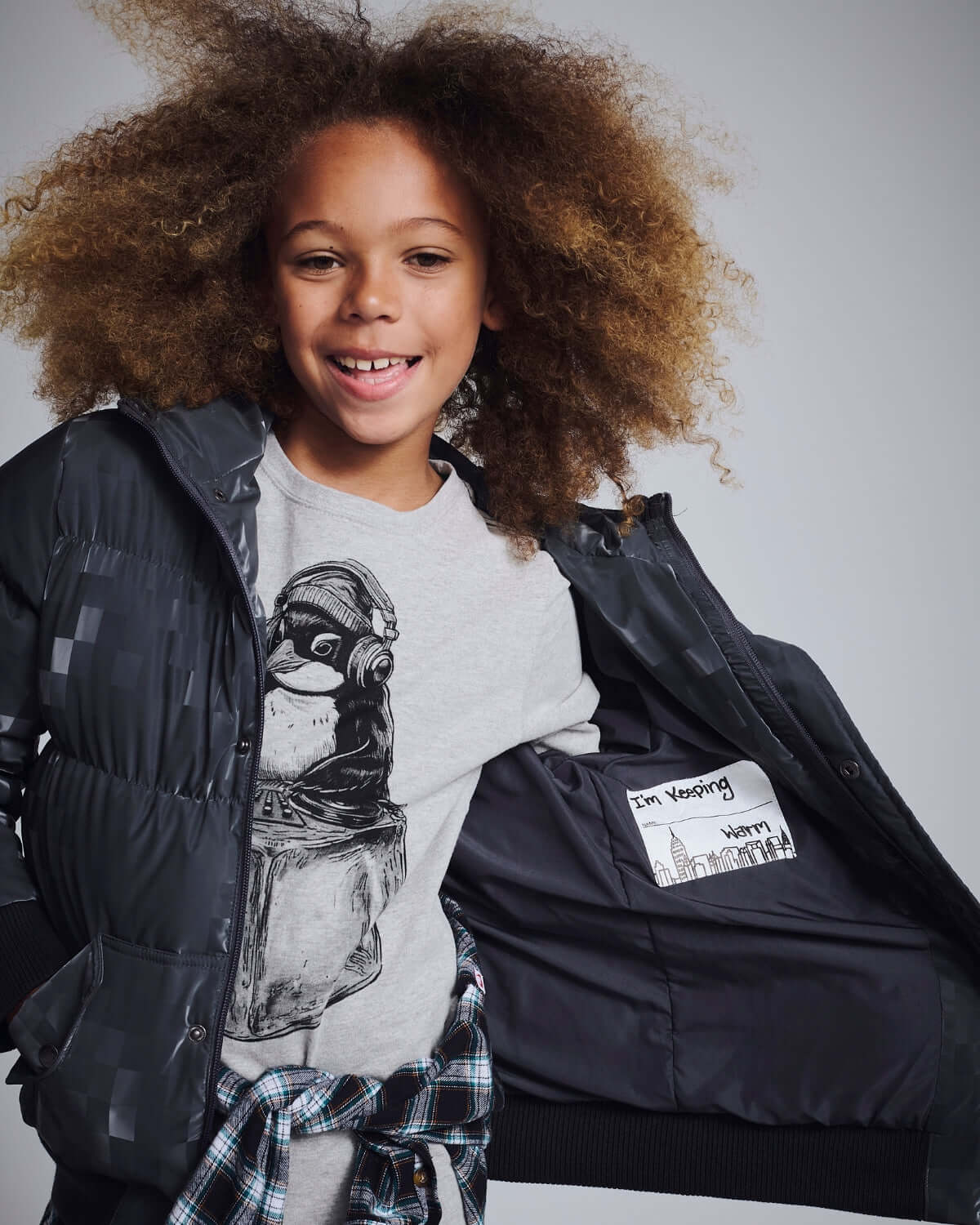 Child wearing a Digital Black Slim Puffy Coat showing inner pockets and a stylish graphic shirt underneath.