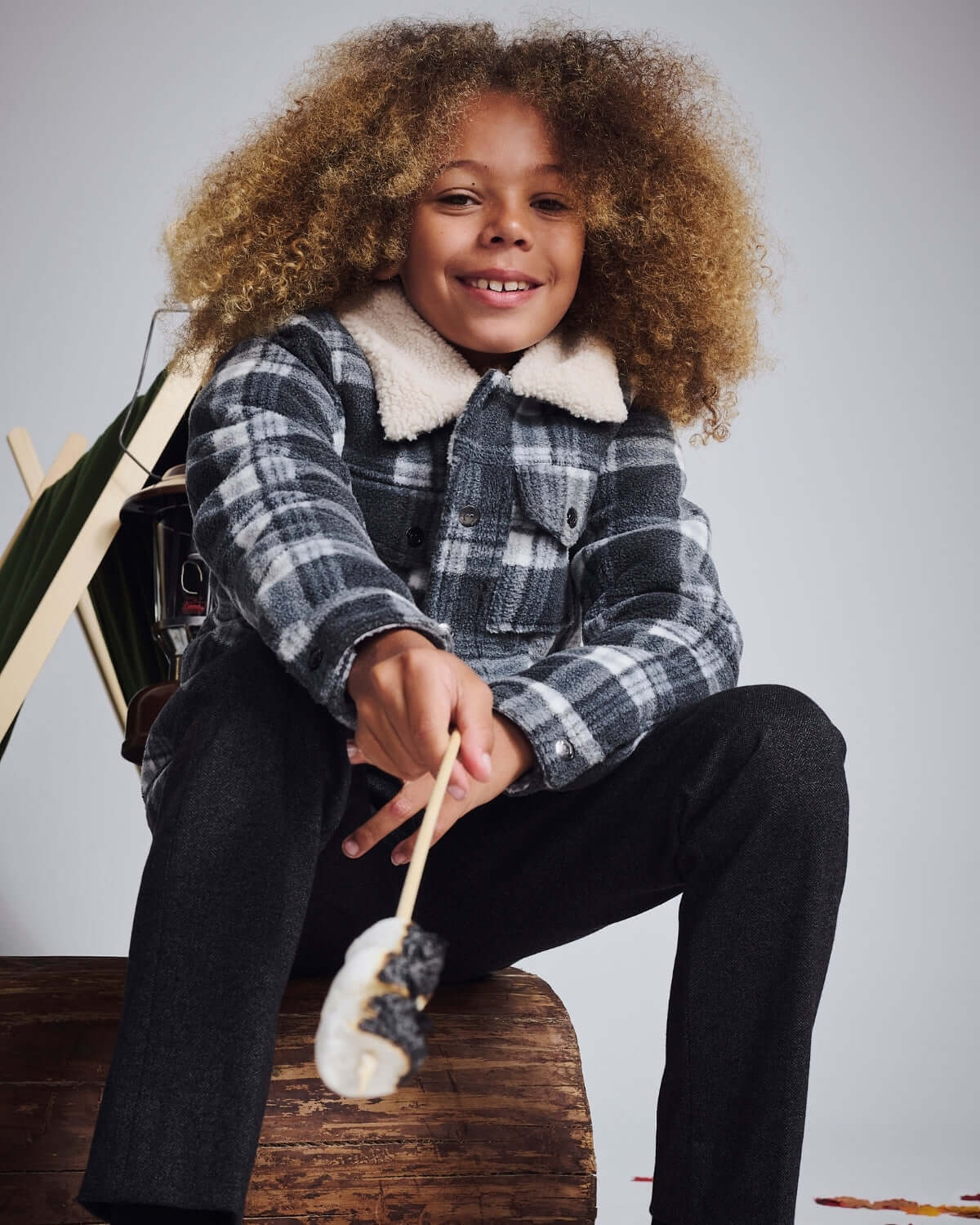 Child in a cozy plaid jacket, wearing Tweed Everyday Stretch Pants, enjoying a marshmallow treat.