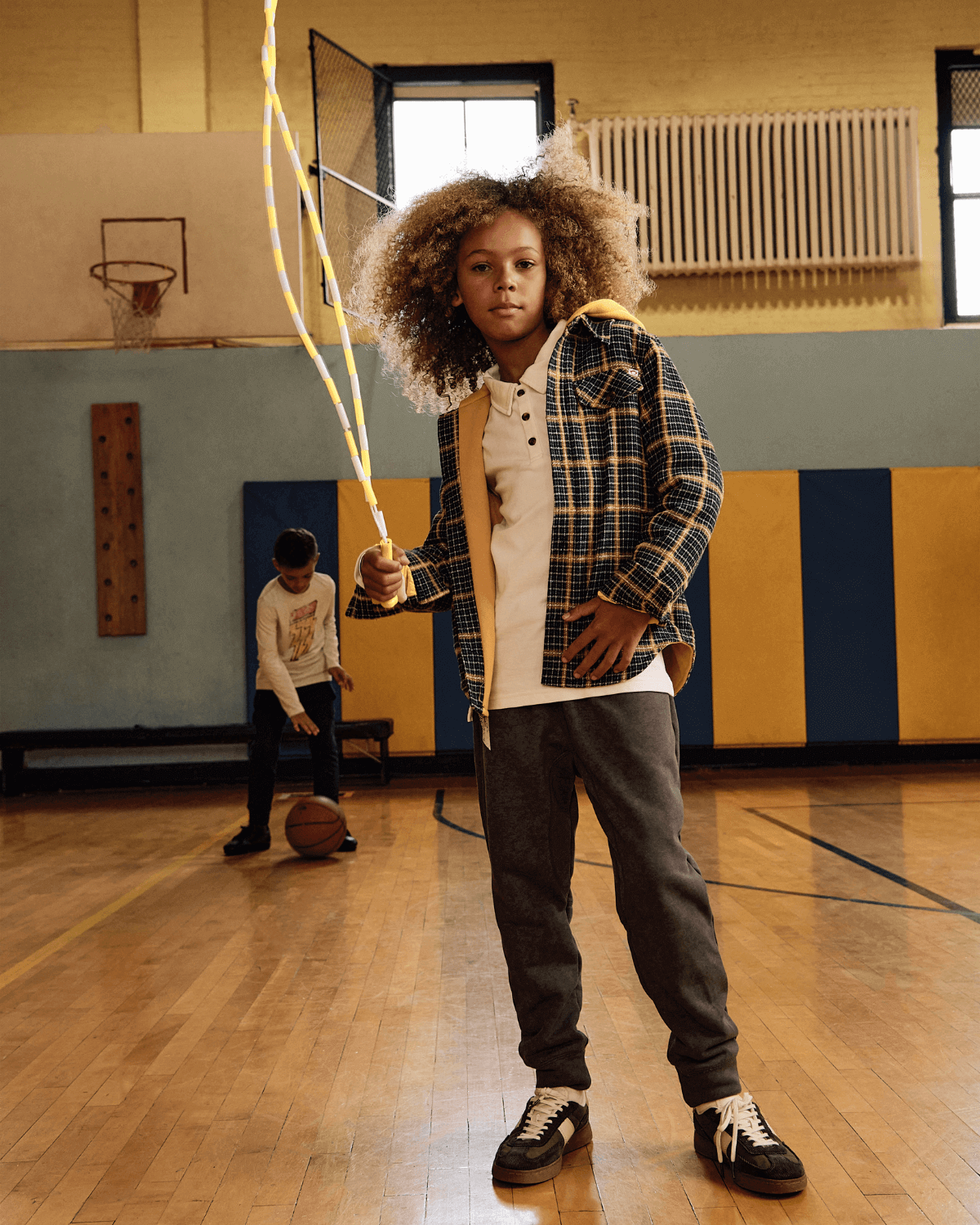 Kid wearing Washed Grey Lightning Sidewalk Sweatpants in a gym, holding jump ropes with a playful look.