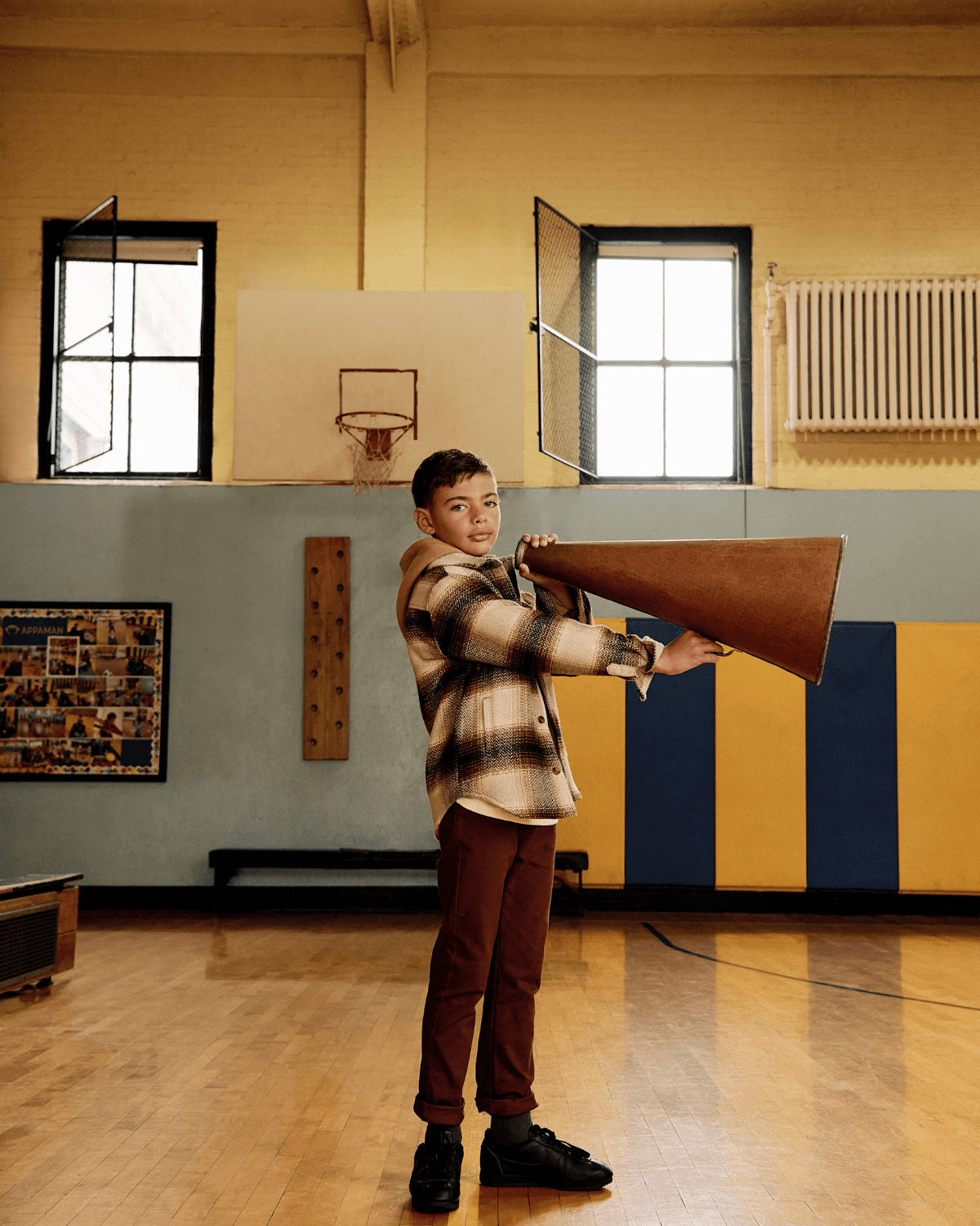 Boy wearing Lumber Plaid Glen Flannel Hoodie holding a megaphone in a gym with blue and yellow walls.