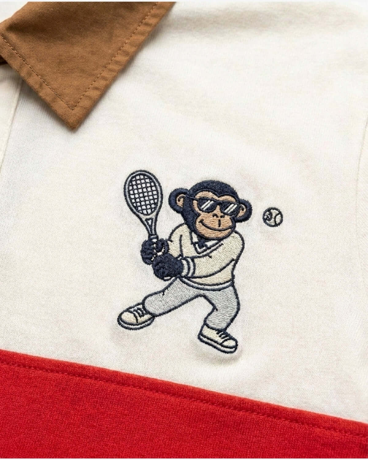 Embroidered monkey holding a tennis racket on a garment with brown and red accents.