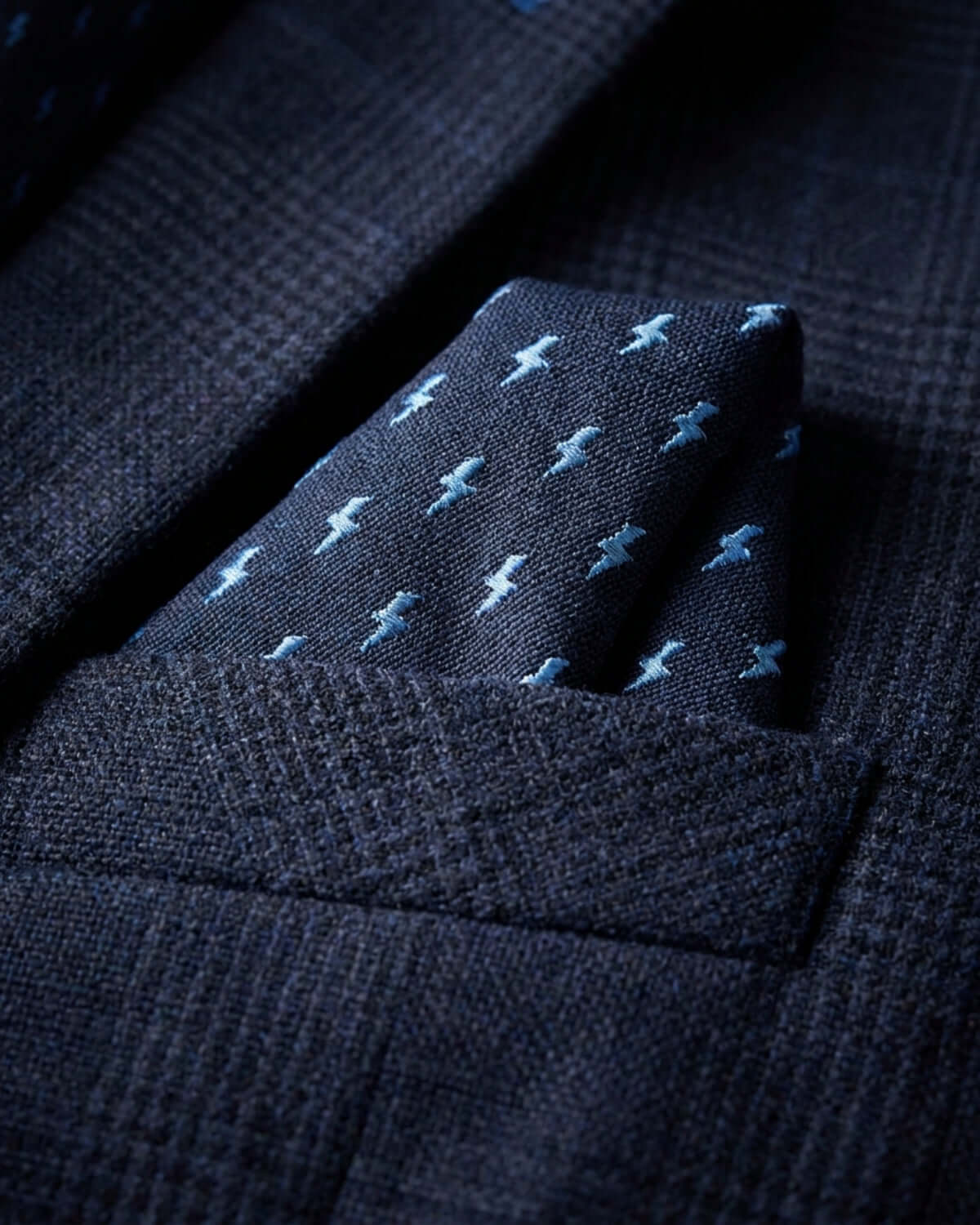 Navy suit with a pocket square featuring small white airplane patterns.