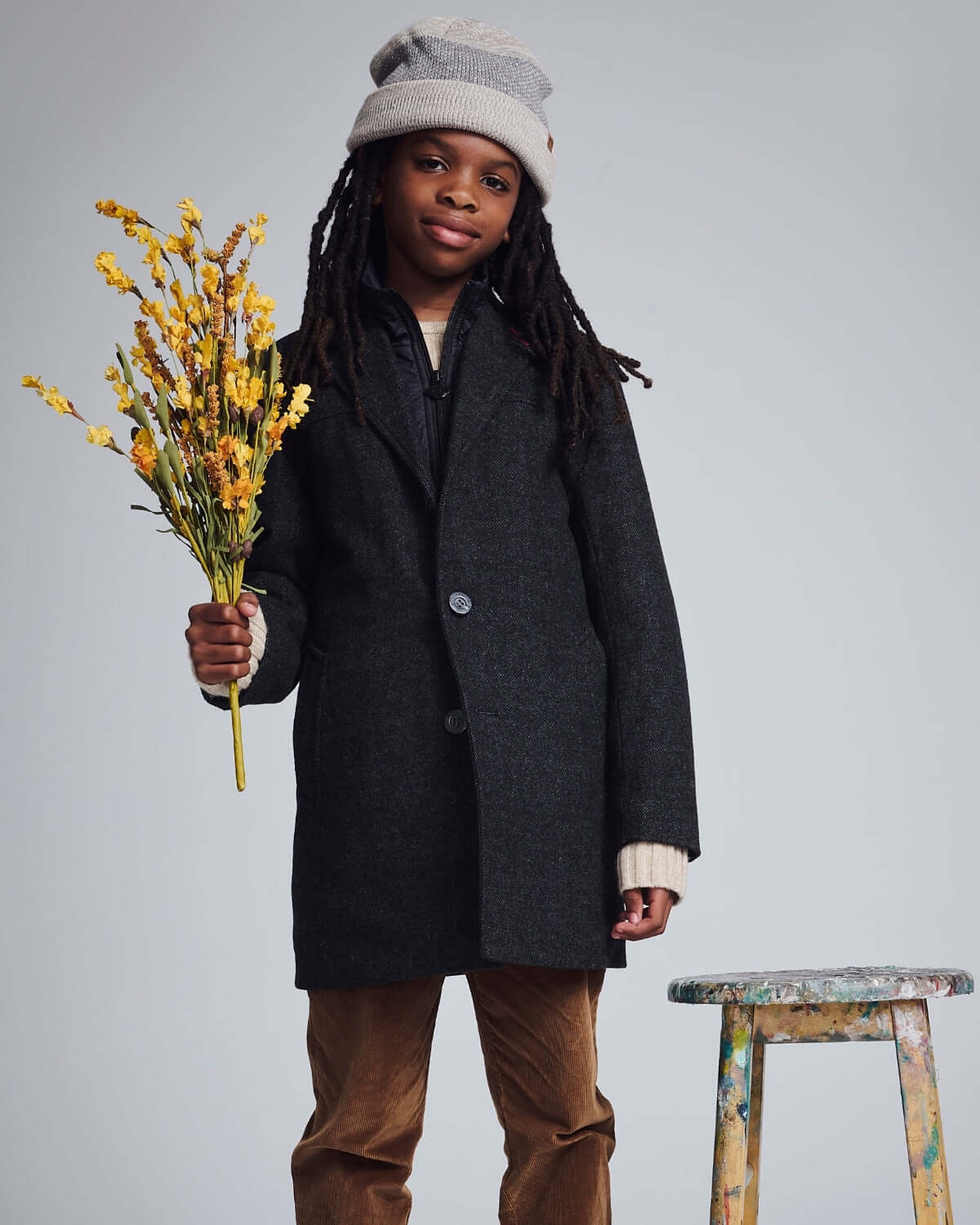 Child wearing a Black Tweed New City Overcoat while holding flowers, showcasing stylish cold-weather fashion.