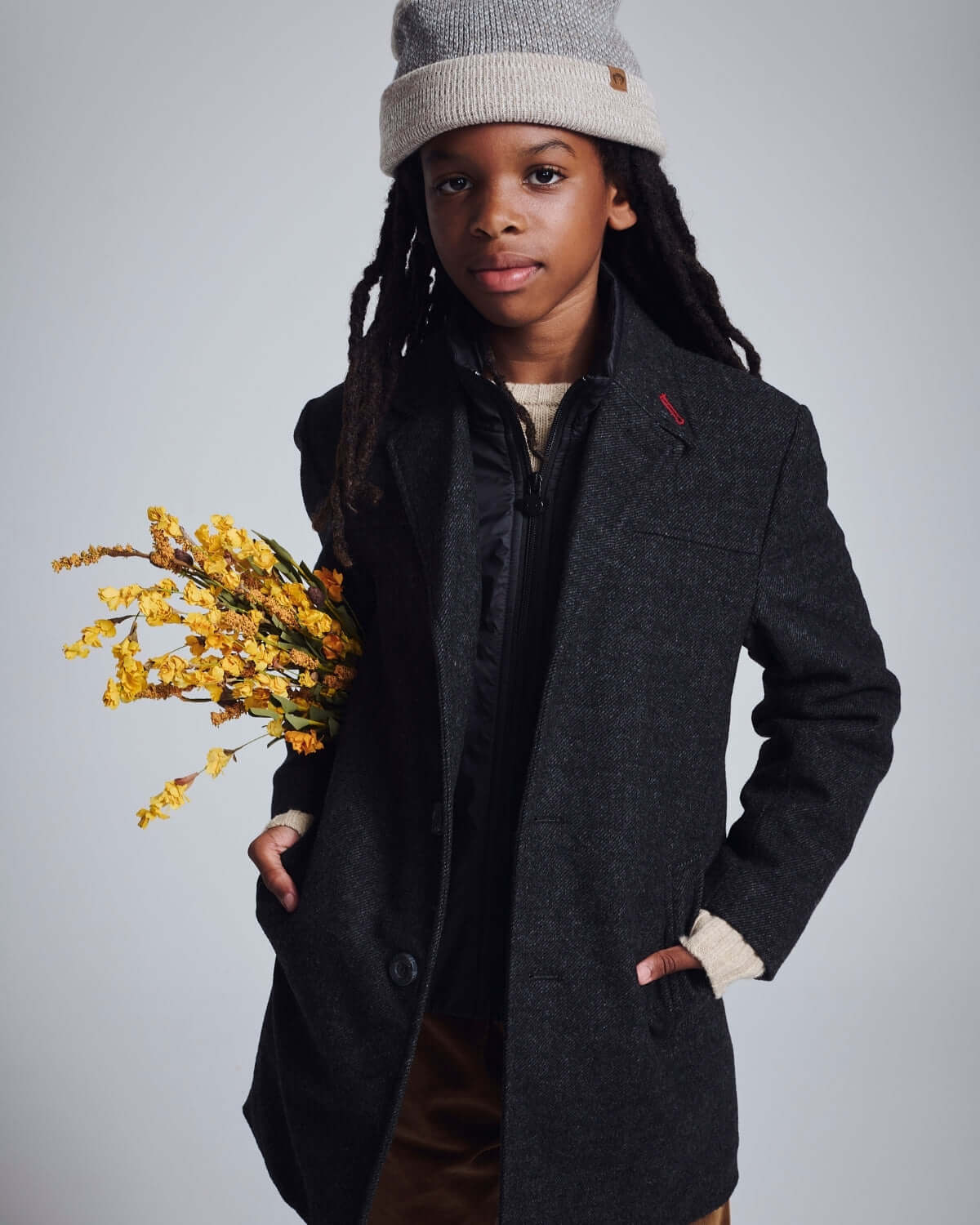Child wearing a Black Tweed New City Overcoat, holding flowers, styled for a polished winter look.
