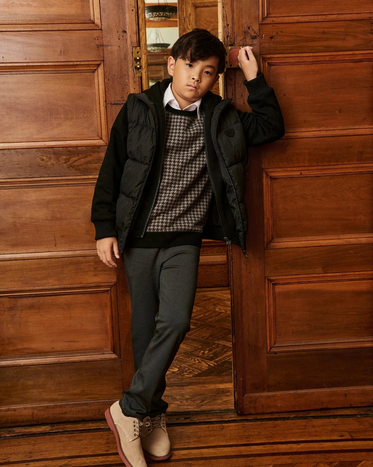 A boy walking outdoors wearing a black hooded jacket, alternate view. Appaman Fall/Winter 2026 collection.