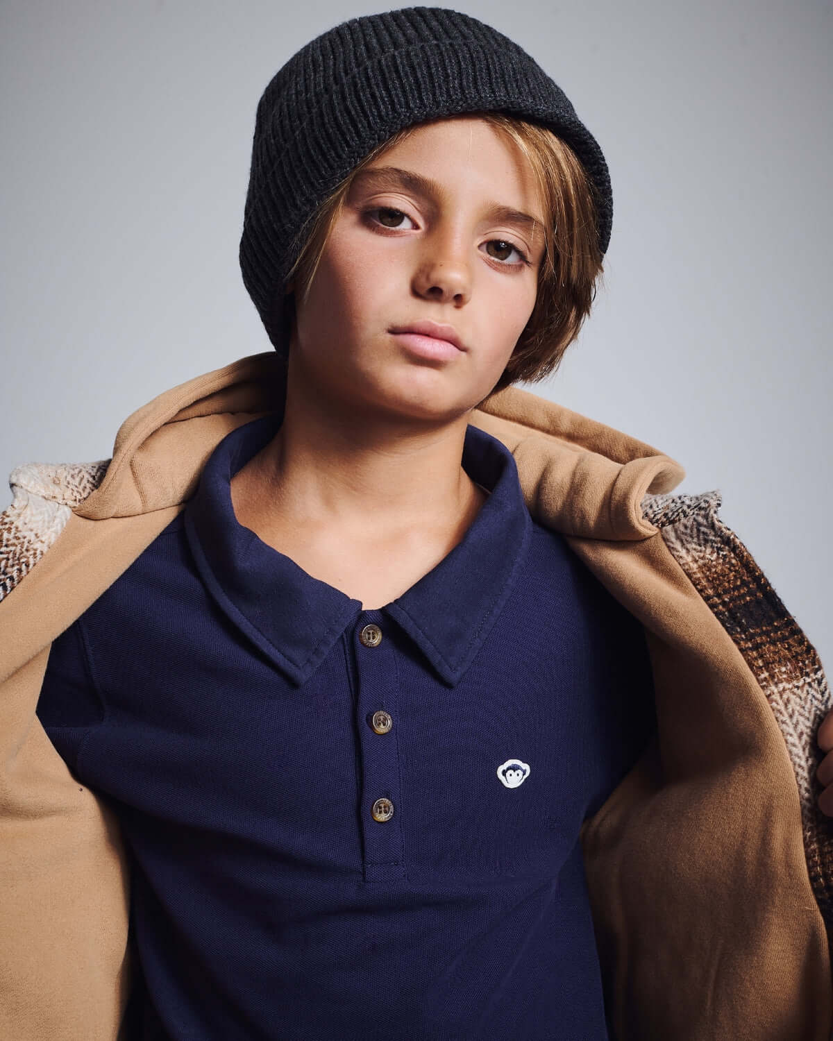 Boy wearing a Navy Blue Parker Polo with a black beanie and a tan jacket.