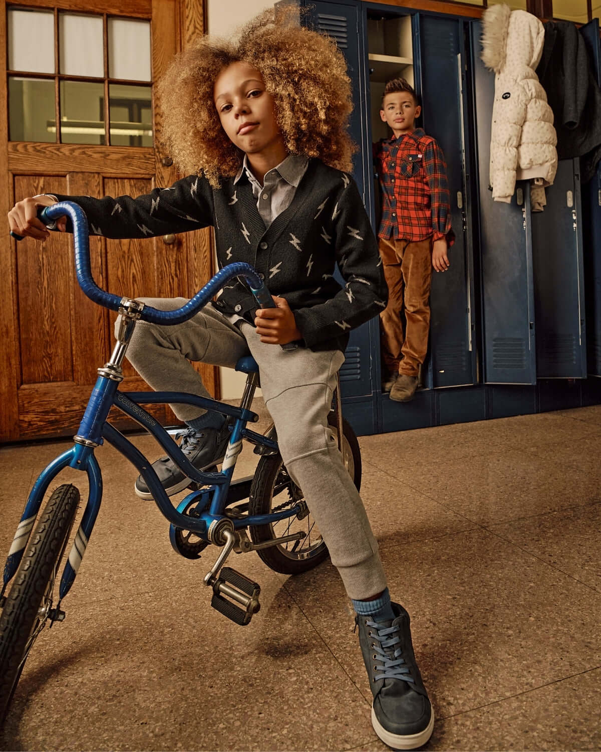 Kids wearing Novelty Grey Heather Sideline Sweatpants and casual outfits, posing with a bike near lockers.