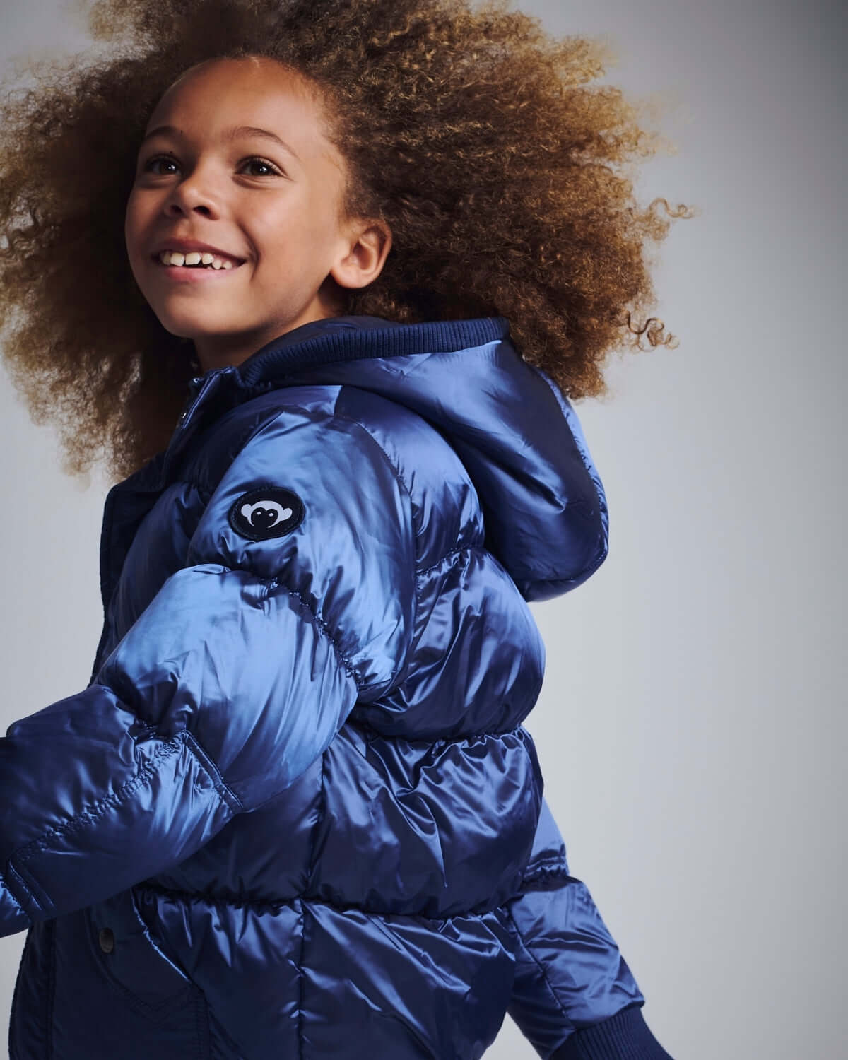 Child wearing a stylish navy blue slim puffy coat with a hood and curly hair, showcasing warmth and comfort.
