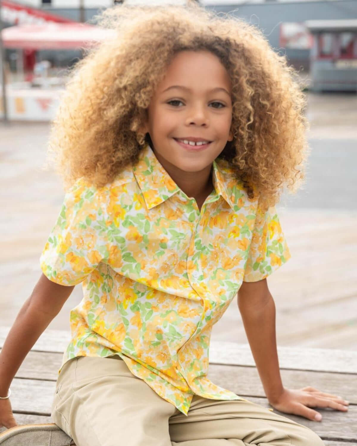 Bright boy in Spring Bouquet Day Party Shirt sitting outdoors with a cheerful smile and colorful floral design.