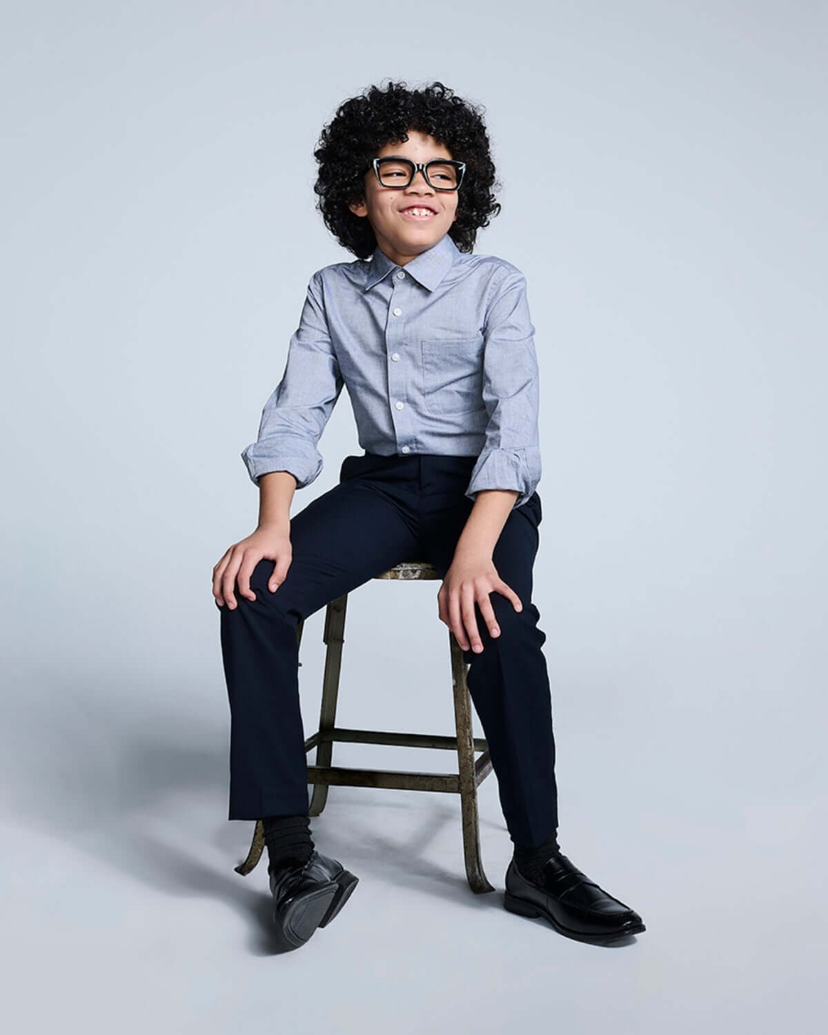 Boy wearing a Grey Standard Button Down shirt sitting on a stool, showcasing stylish outfit with tailored pants.
