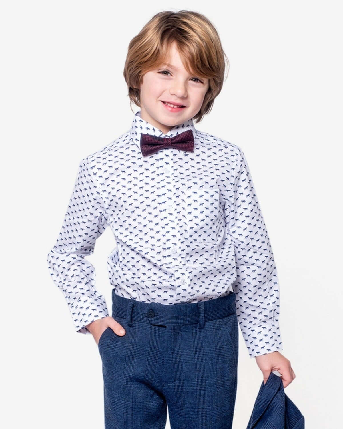 A young boy wearing The Pointer Standard Button Down dress shirt with a playful dog print and a bow tie.
