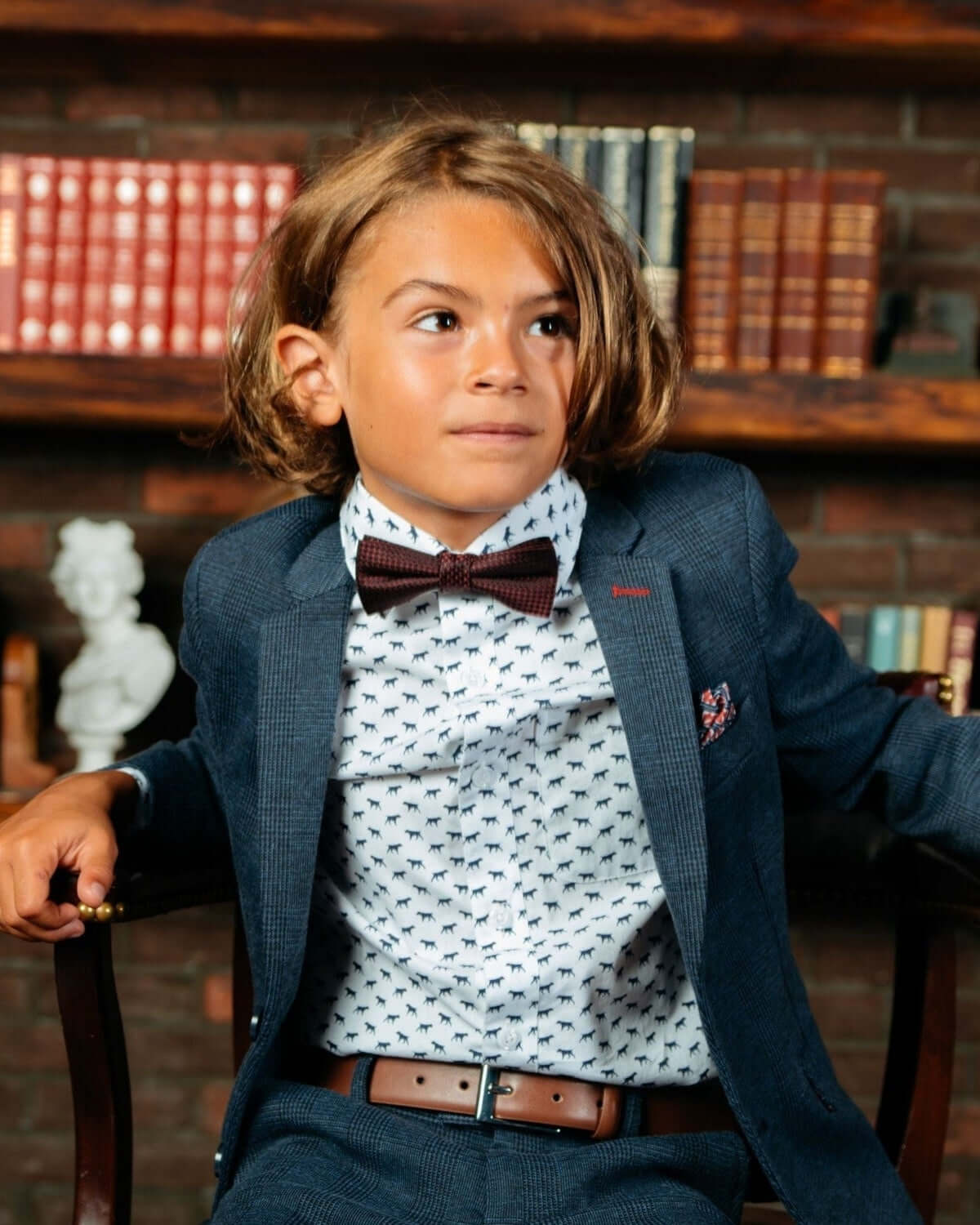 A young boy wearing The Pointer Standard Button Down shirt with a playful dog print and a bow tie.