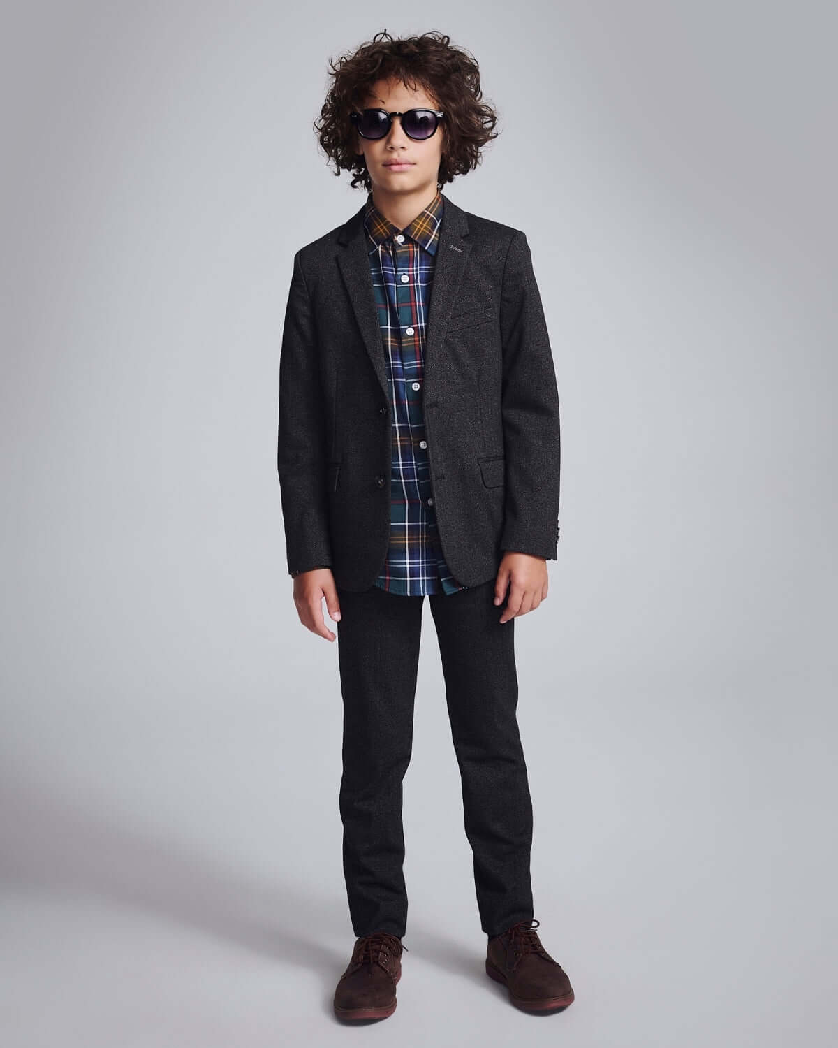Black Herringbone Stretchy Suit Pants worn by a stylish boy with curly hair and sunglasses.