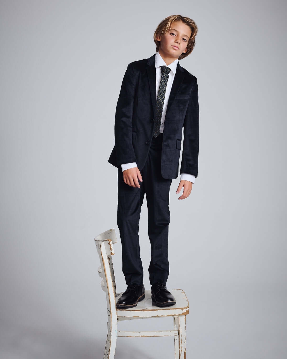 Young boy modeling the Midnight Velvet Plaid Suit Pants with a stylish suit and tie, standing on a chair.