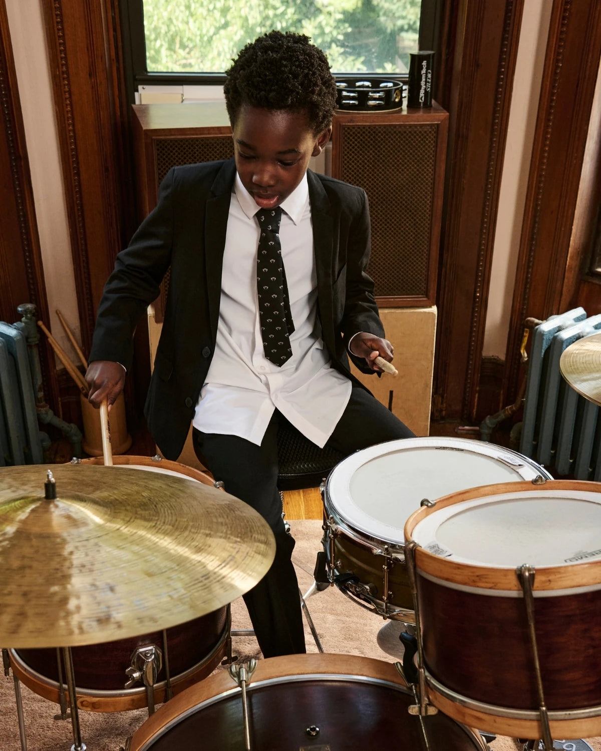 A child wearing an ivory tuxedo jacket, playing drums. Appaman Fall/Winter 2026 collection.