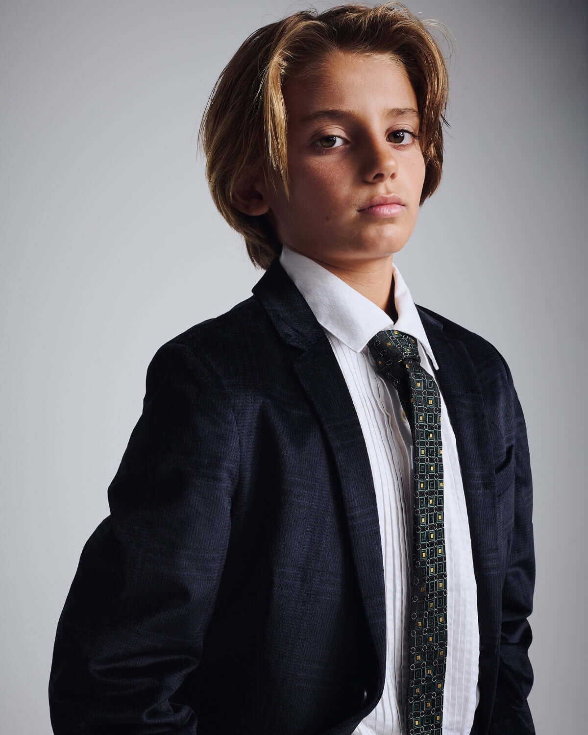 A stylish young boy wearing a black suit and Gold Spruce Tie from Appaman’s Fine Tailoring Collection.