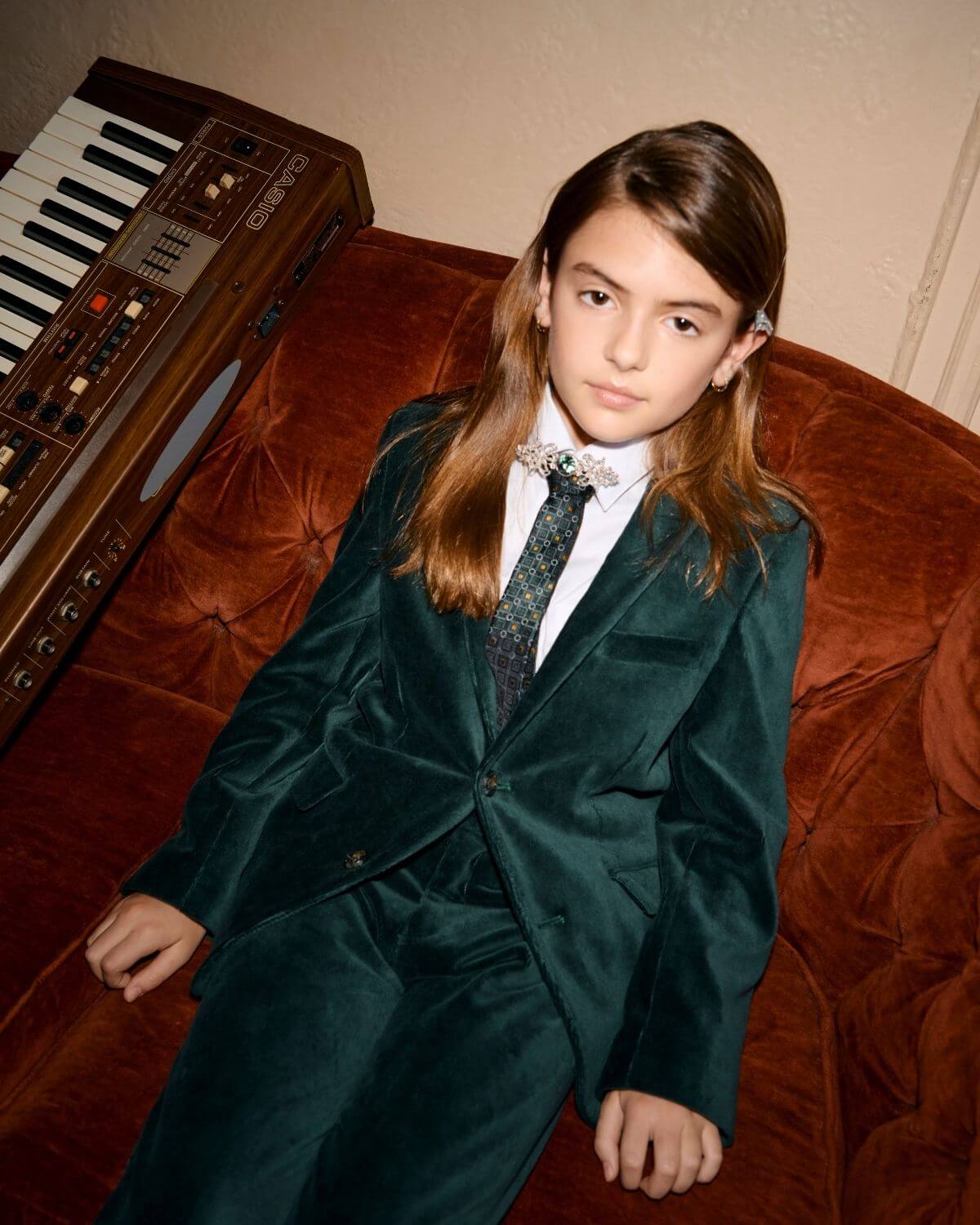 Child wearing an Evergreen Velvet Blazer, exuding style and charm against a vintage keyboard backdrop.