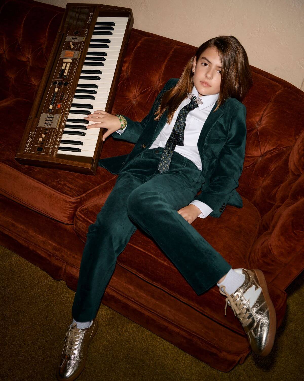 Child wearing Evergreen Velvet Suit Pants, styled with a white shirt and tie, sitting beside a vintage keyboard.