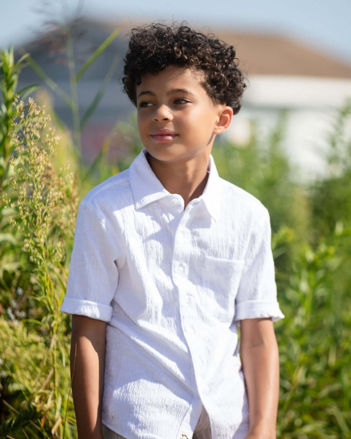 Boy wearing a White Beach Shirt, enjoying the sun surrounded by greenery.