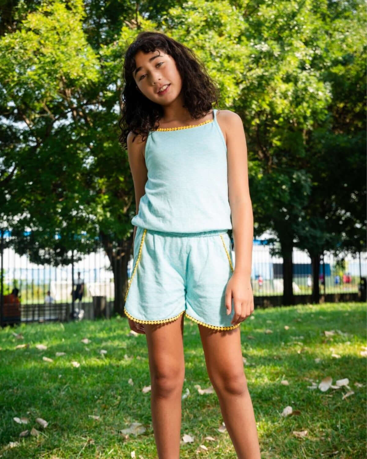 Aqua Novia Romper on a girl playing outside in a park, showcasing playful yellow detailing and vibrant color.
