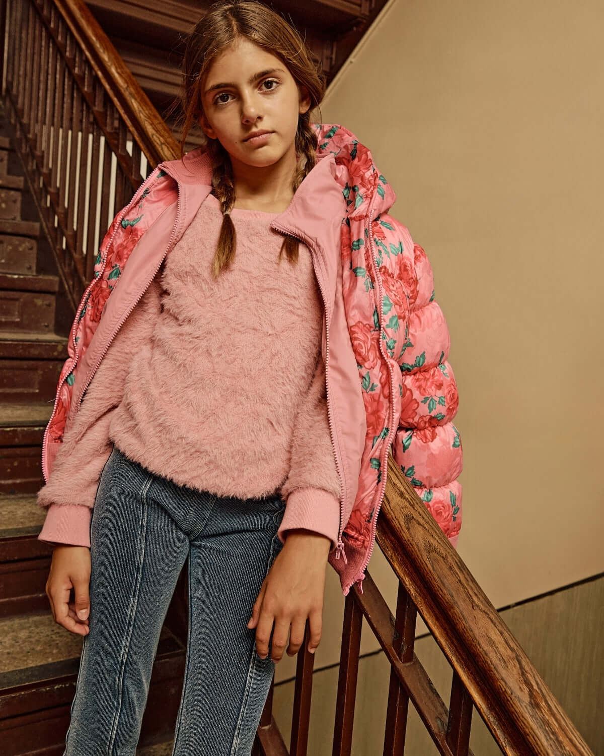 Girl in a pink fluffy sweater and floral pink puffer jacket standing on stairs, showcasing stylish winter fashion.