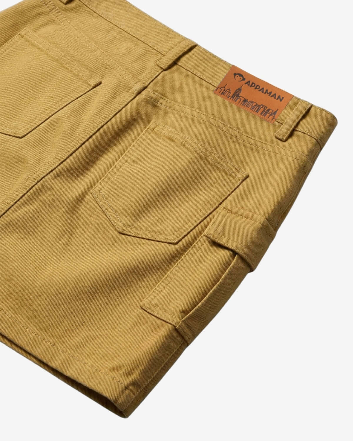 Folded mustard yellow pants with a brand label on a white background
