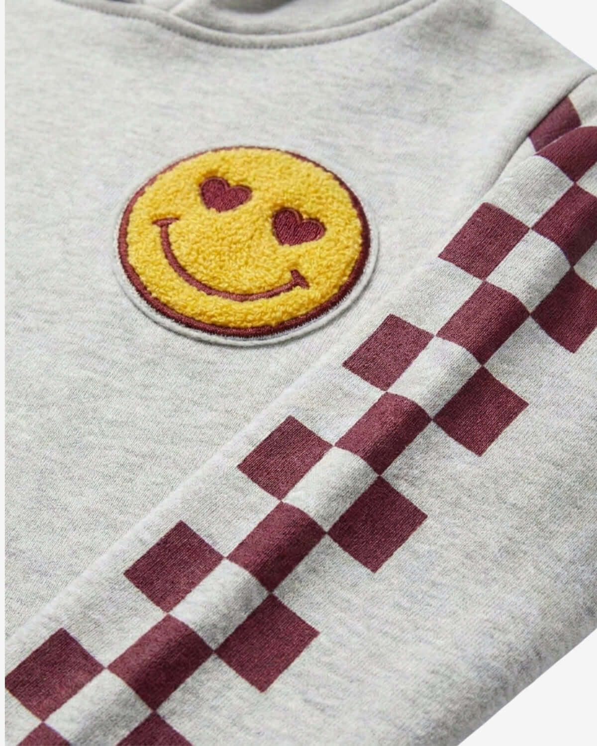 Gray sweatshirt with a yellow smiley face patch and red and white checkered pattern.