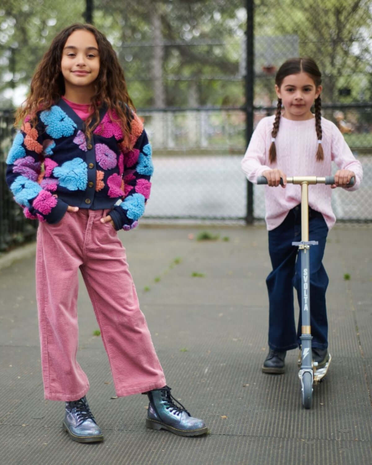 Two kids playing outside, one wearing Dusty Rose Liana Jeans and a colorful cardigan, the other on a scooter.
