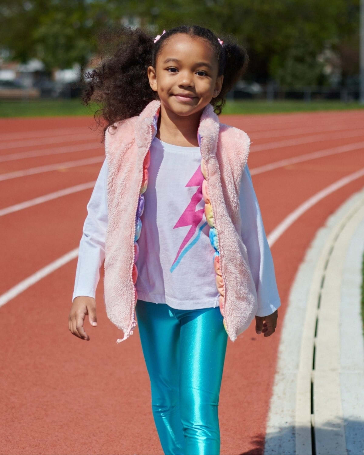 Girl wearing Lightning Bolt Adler Tee with bright leggings on a running track, radiating joy and style.