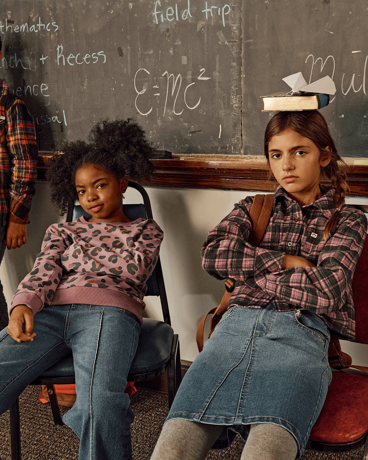 Two kids sitting in a classroom wearing comfortable styles, featuring a Midi Denim Skirt and playful sweaters.