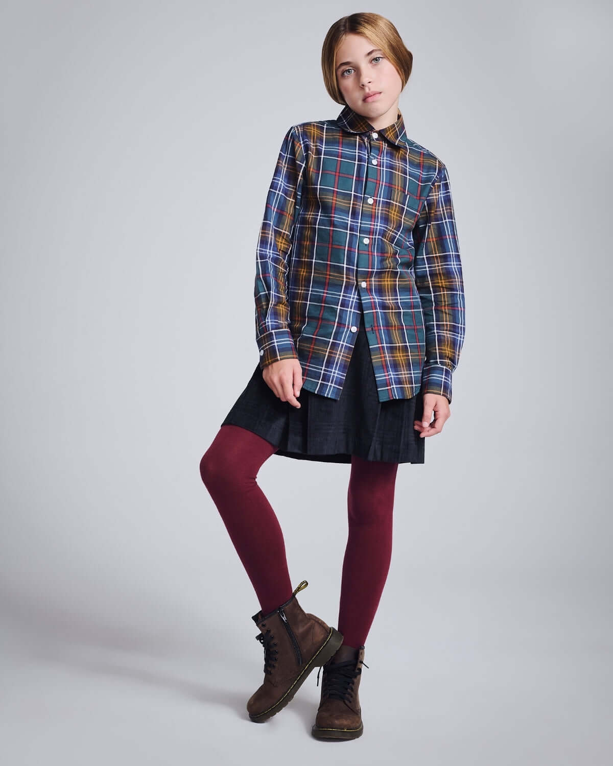 Child wearing a plaid shirt with Midnight Velvet Plaid Pleated Skirt and maroon leggings, perfect for a stylish outfit.