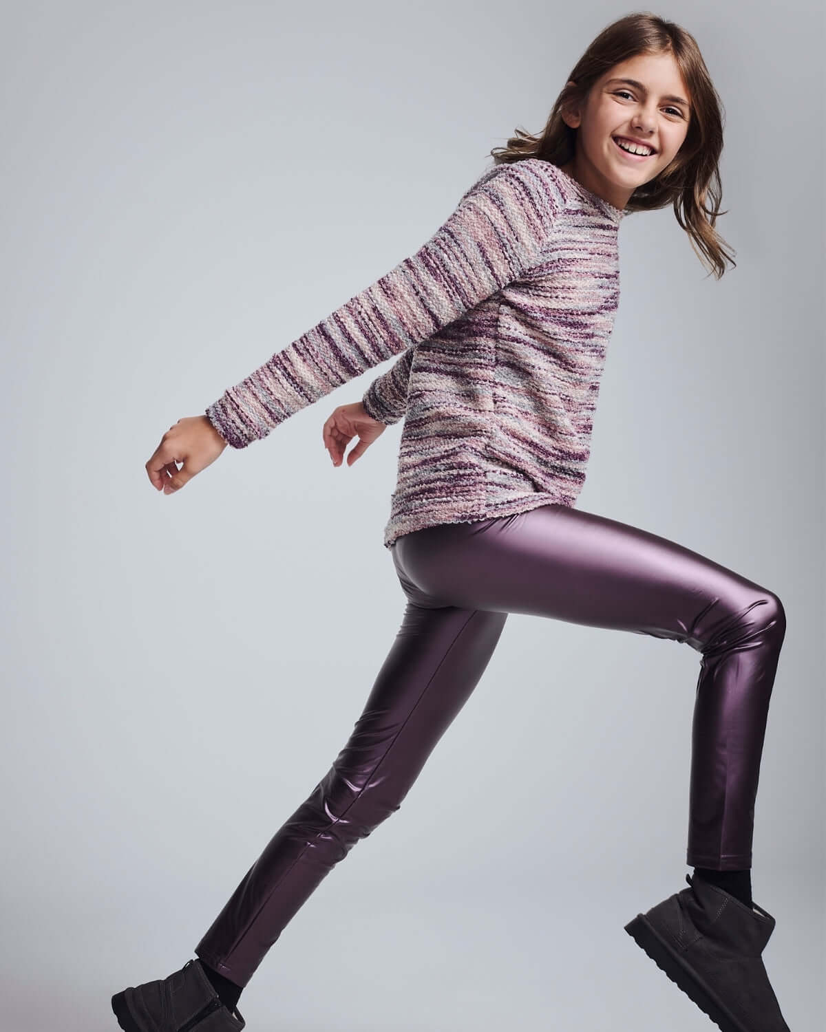 Girl wearing Purple Shine Leggings, smiling and dancing in a colorful sweater, showcasing vibrant kids' fashion.