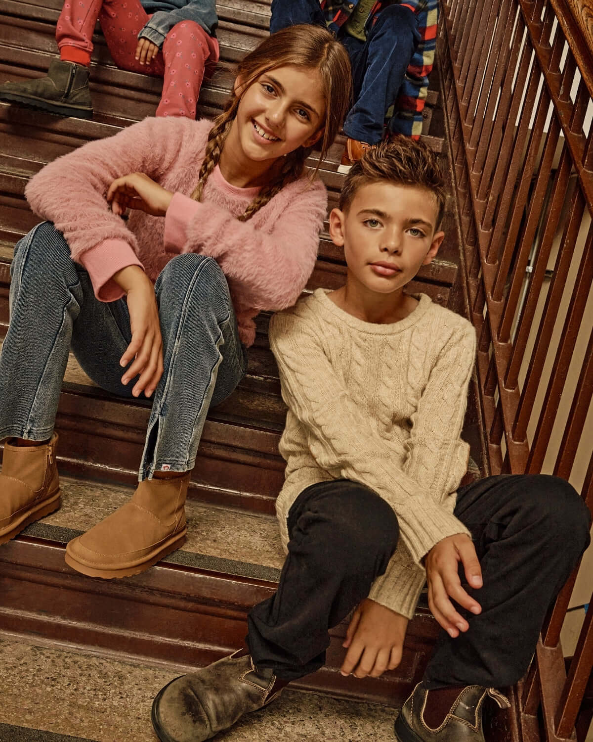 Kids wearing the Ivy Rose Willow Top and cozy sweaters sitting on stairs, showcasing stylish children's fashion.