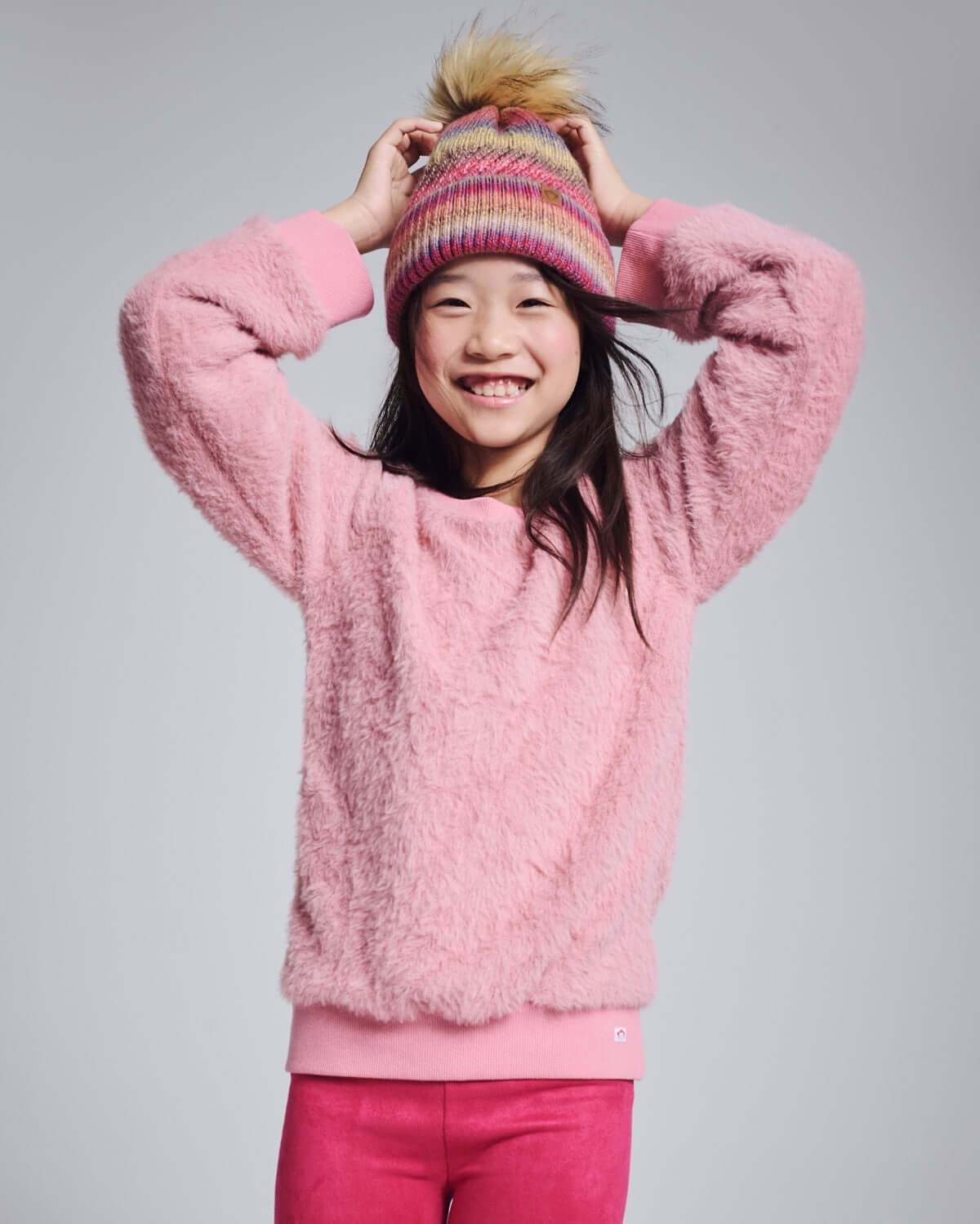 A cheerful girl wearing the Ivy Rose Willow Top in soft pink, with a colorful hat, smiling happily.