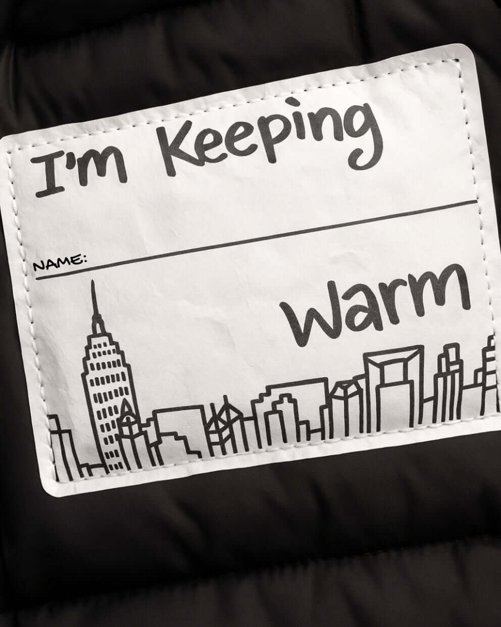 Kids Black Puffy Coat label showing "I'm Keeping Warm" with city skyline design.