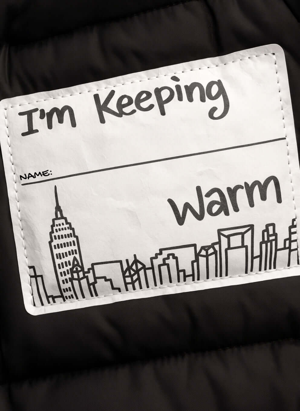 Kids Black Puffy Coat label showing "I'm Keeping Warm" with city skyline design.