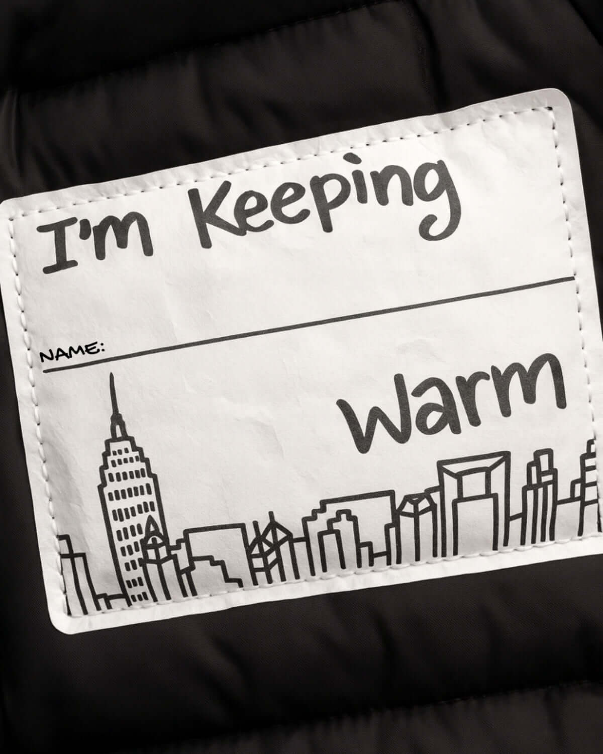 Label on Black Park Ave Long Puffer jacket saying "I'm Keeping Warm" with NYC skyline illustration.