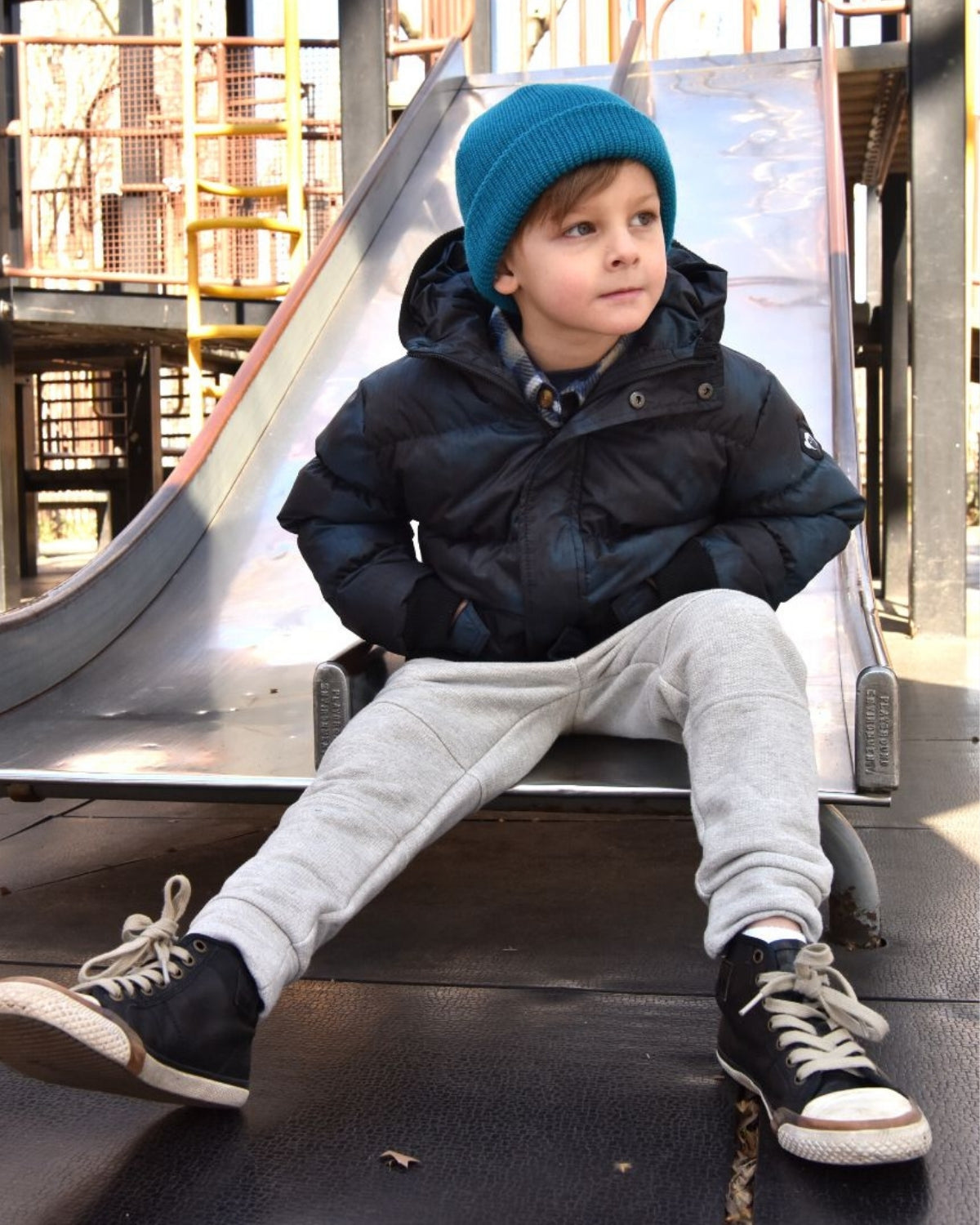 Stylish kid in a cozy black puffer jacket and aqua haze hat, ready for winter fun at the playground.