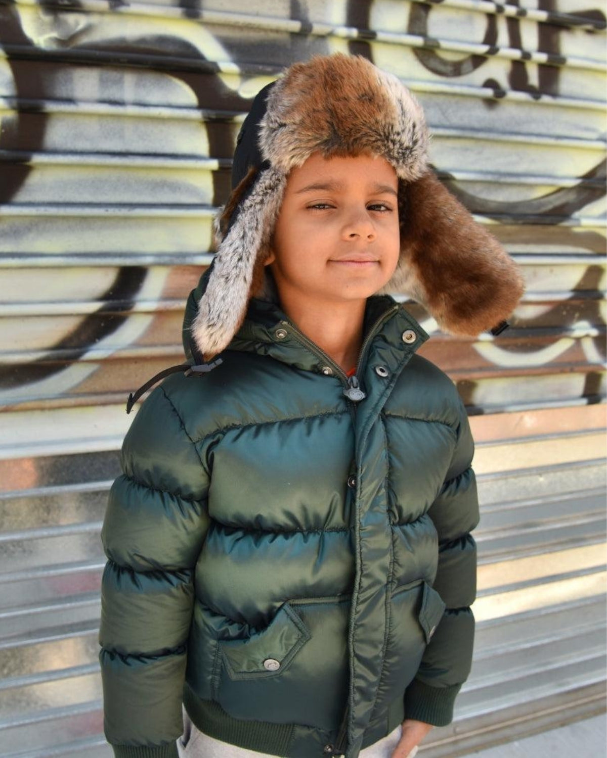 Stylish kid rocking a cozy green puffer jacket and a chic faux fur-lined black Benji hat, ready for winter adventures!