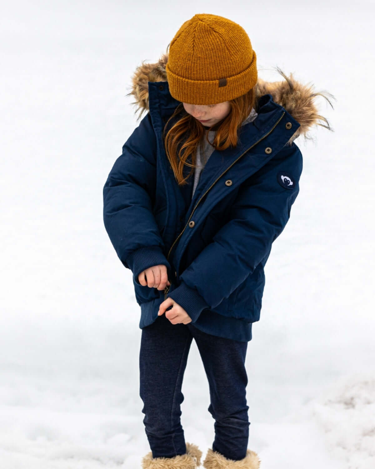 Adorable kid bundled up in a navy puffer coat and golden spice hat, ready for snowy adventures in style!