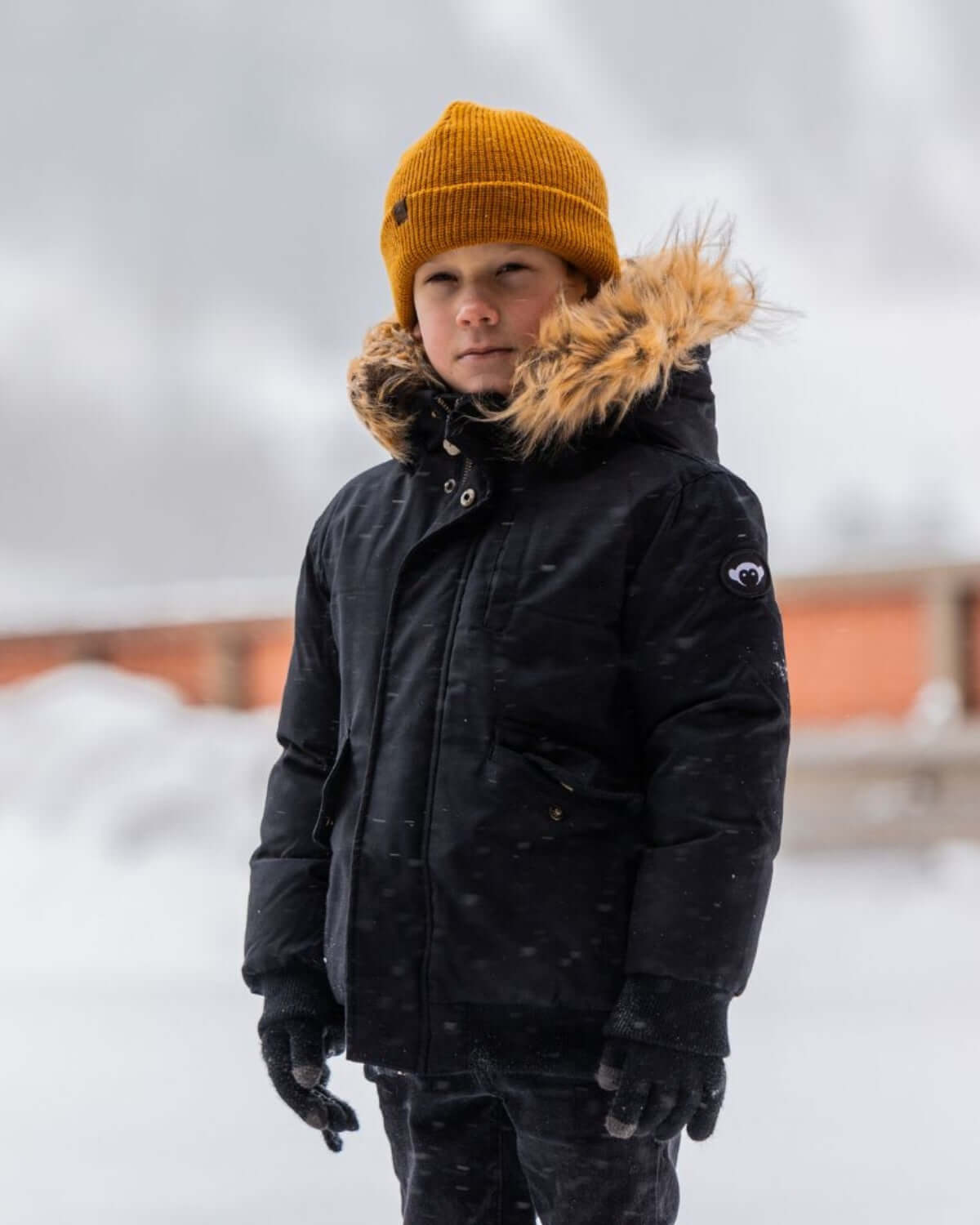 Stylish kid in a black winter coat and a golden beanie, ready for snowy adventures—a perfect choice for back-to-school fun!