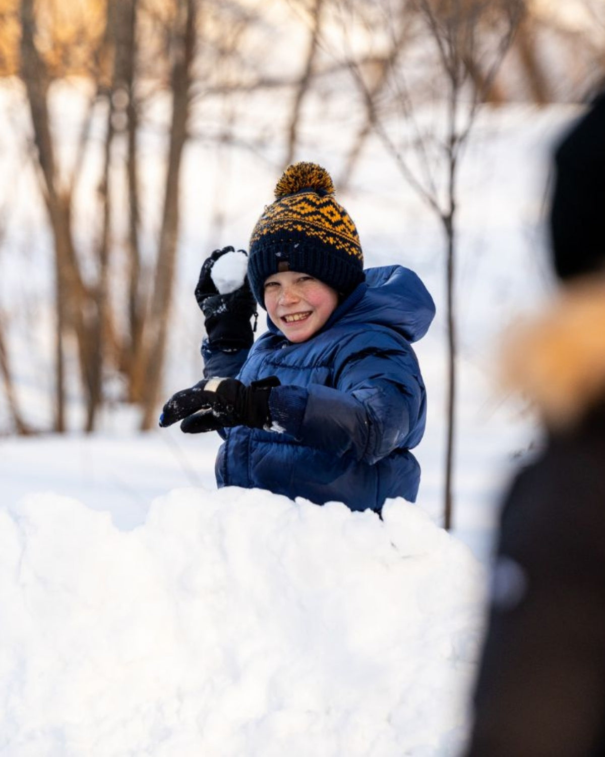 Joyful boy in a cozy navy blue bush hat, throwing snowballs in winter wonderland—fun kids clothes for stylish outdoor adventures!