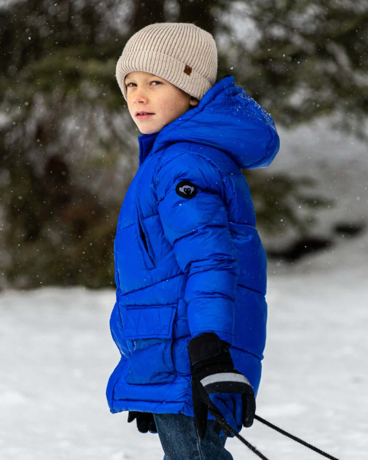 Stylish boy in a bright blue puffer jacket with a cozy tan beanie enjoying snowy adventures—perfect kids clothes for back to school!