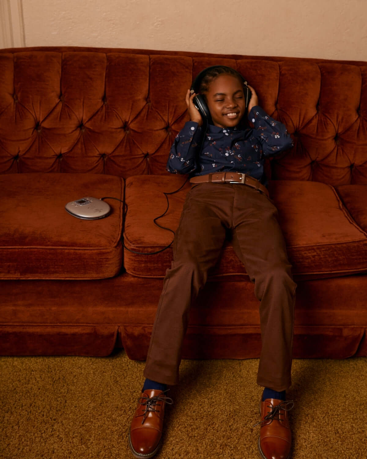 A happy kid in brown commuter twill pants, enjoying music on a cozy couch, showcasing stylish kids clothes for playtime.