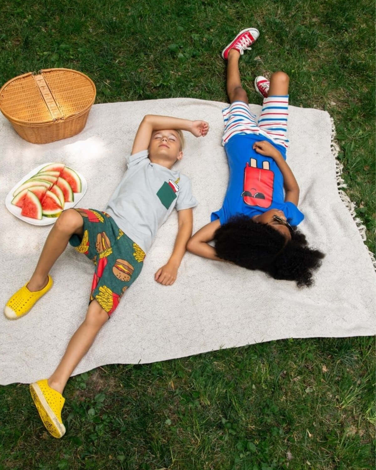 Kids lounging on a blanket wearing Burgers & Fries Camp Shorts and colorful tees during a summer picnic.