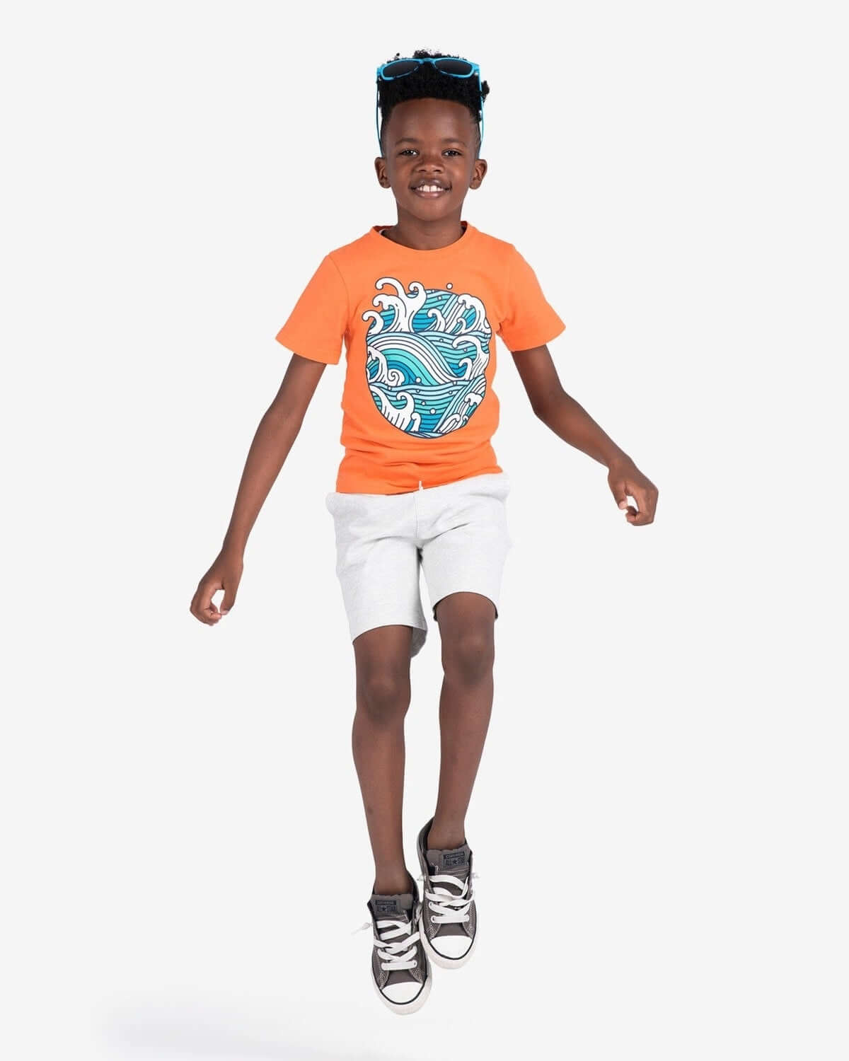 Happy boy jumping in vibrant orange shirt and light shorts, showcasing stylish kids clothes for back to school fun!